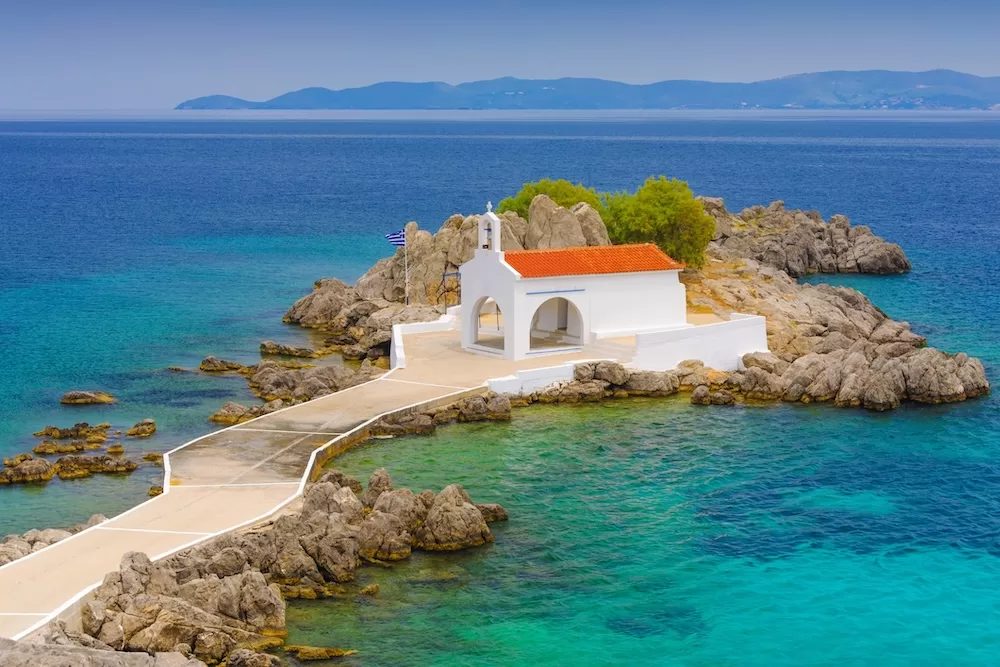 A classical white greek church on a small rocky island in Agios Isidoros, Greece. 