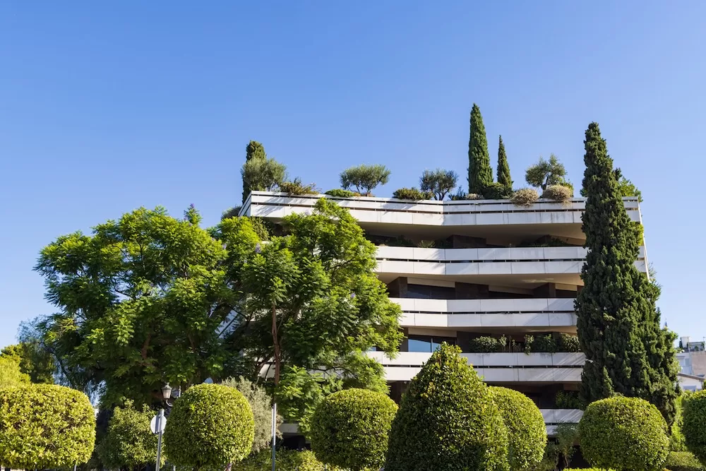 A modern apartment building with a green roof surrounded by trees in the center of Athens, Greece.